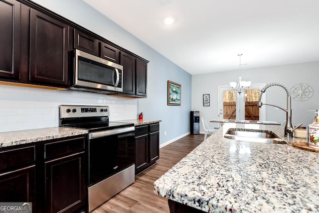 kitchen featuring a sink, light stone counters, backsplash, wood finished floors, and stainless steel appliances