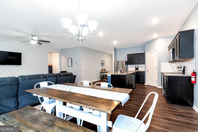 dining room with dark wood finished floors, wallpapered walls, an accent wall, and baseboards