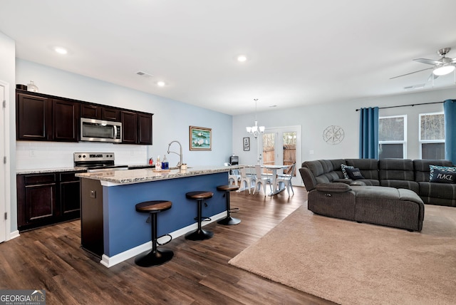 kitchen featuring dark wood-style floors, an island with sink, dark brown cabinetry, appliances with stainless steel finishes, and backsplash