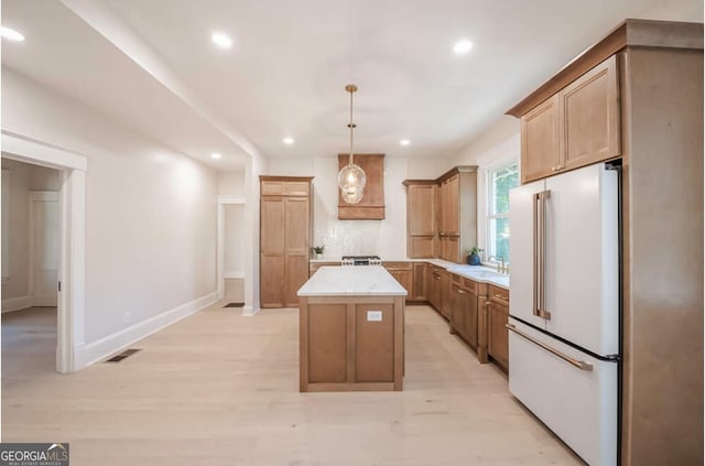 kitchen featuring high end white refrigerator, sink, light hardwood / wood-style flooring, a center island, and hanging light fixtures