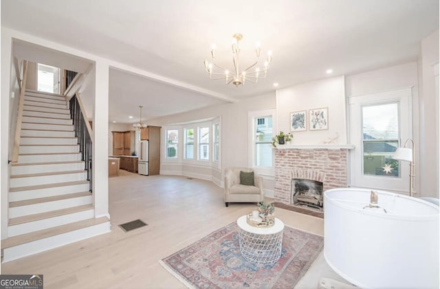 living room featuring a fireplace, light wood-type flooring, an inviting chandelier, and a healthy amount of sunlight