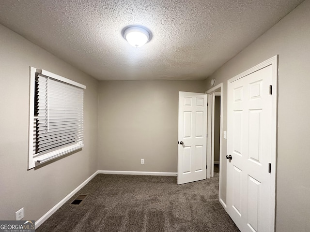 unfurnished bedroom with dark carpet and a textured ceiling