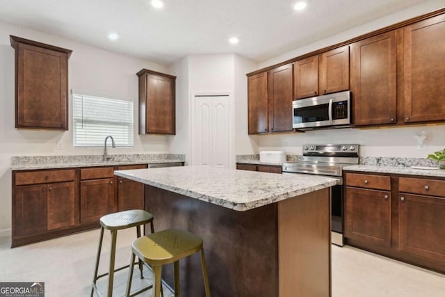 kitchen featuring light stone countertops, a breakfast bar, stainless steel appliances, sink, and a kitchen island