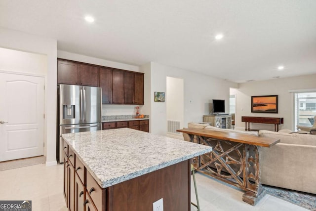 kitchen featuring light stone countertops, stainless steel fridge, a breakfast bar, dark brown cabinetry, and a center island