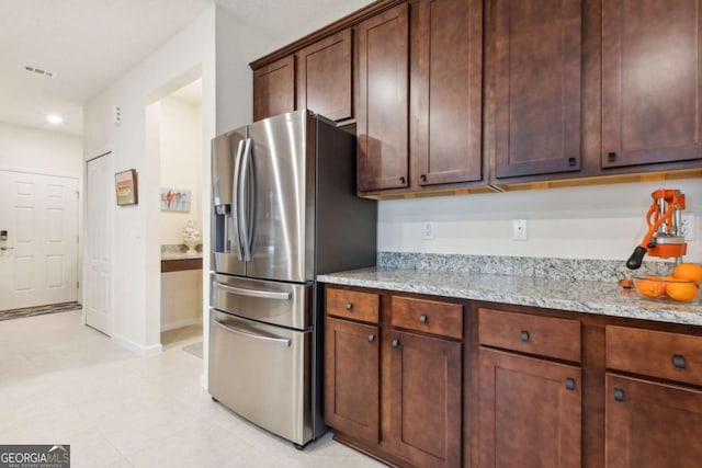 kitchen featuring stainless steel fridge with ice dispenser, dark brown cabinetry, and light stone counters