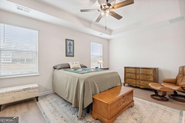bedroom with ceiling fan, light hardwood / wood-style floors, and a raised ceiling