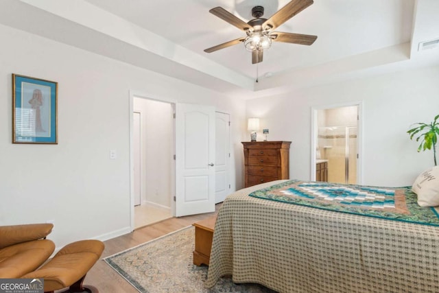 bedroom featuring a tray ceiling, ensuite bath, ceiling fan, and light hardwood / wood-style floors