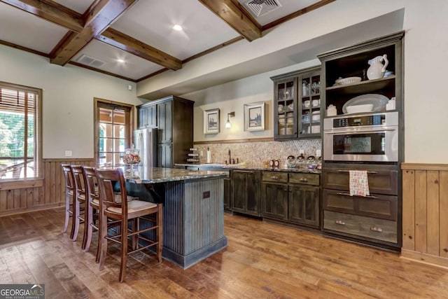 kitchen with a center island, dark stone counters, light wood-type flooring, appliances with stainless steel finishes, and a kitchen bar