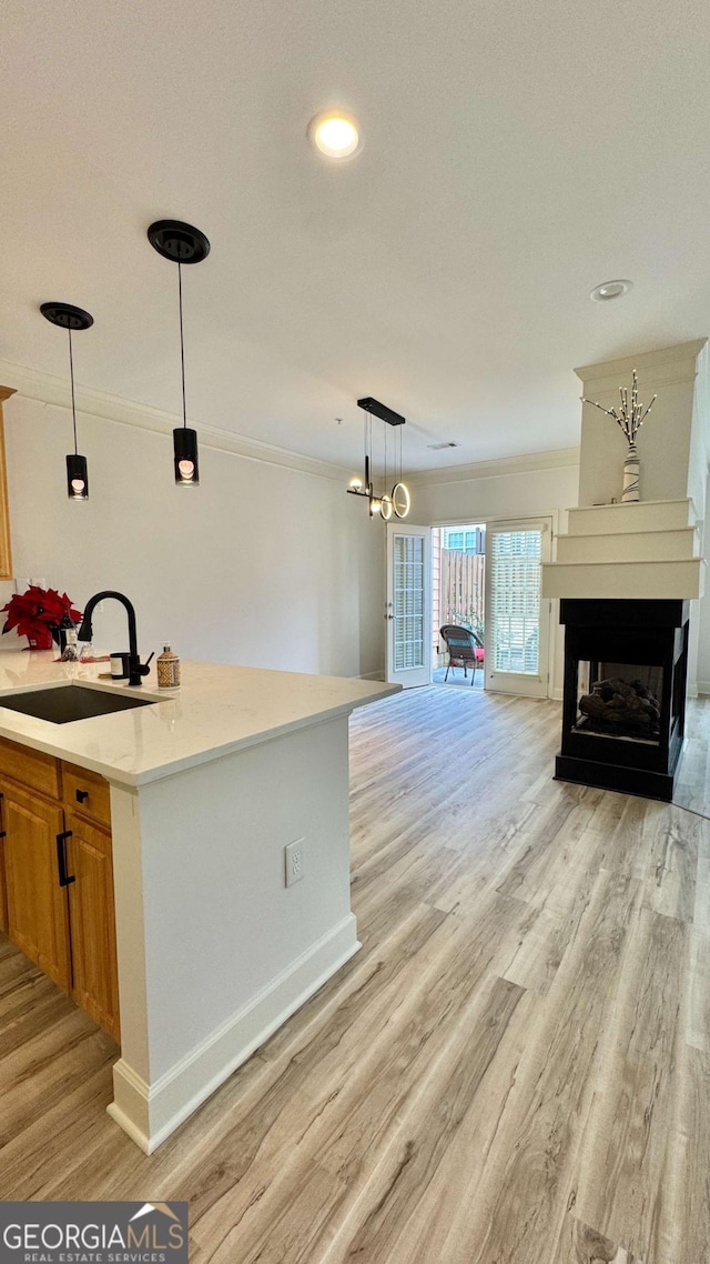 kitchen featuring sink, hanging light fixtures, a multi sided fireplace, crown molding, and light wood-type flooring