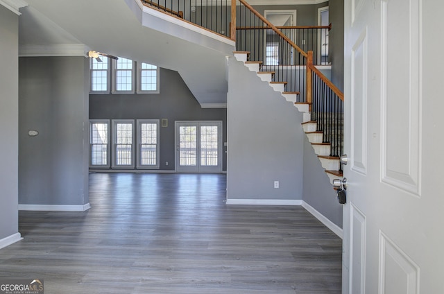 entryway with stairs, a towering ceiling, baseboards, and wood finished floors