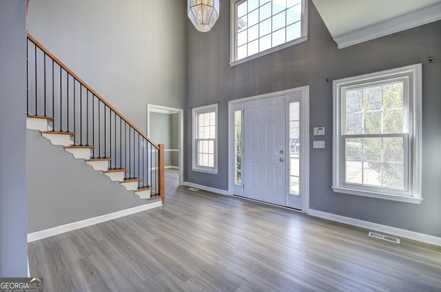 entrance foyer featuring wood finished floors, a towering ceiling, visible vents, baseboards, and stairway