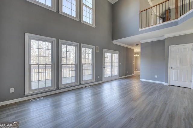 unfurnished living room with visible vents, a towering ceiling, baseboards, and wood finished floors