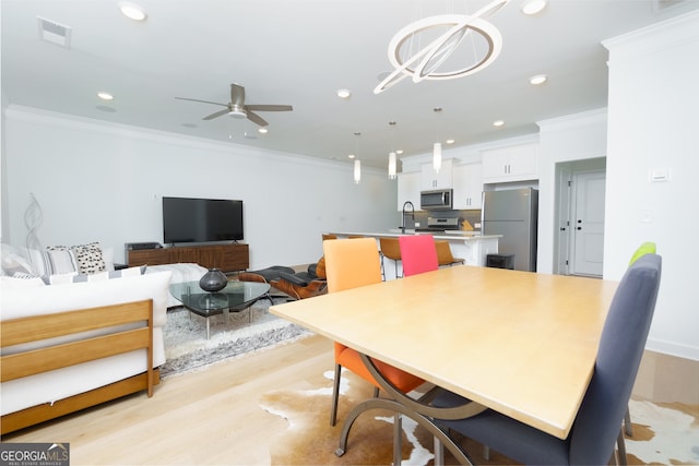 dining space featuring ceiling fan with notable chandelier, ornamental molding, sink, and light hardwood / wood-style flooring