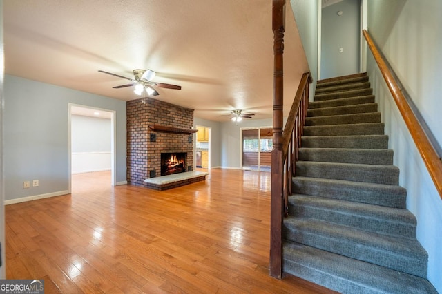 staircase with hardwood / wood-style floors, ceiling fan, and a fireplace