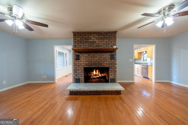 unfurnished living room featuring a wealth of natural light, ceiling fan, light hardwood / wood-style floors, and a brick fireplace