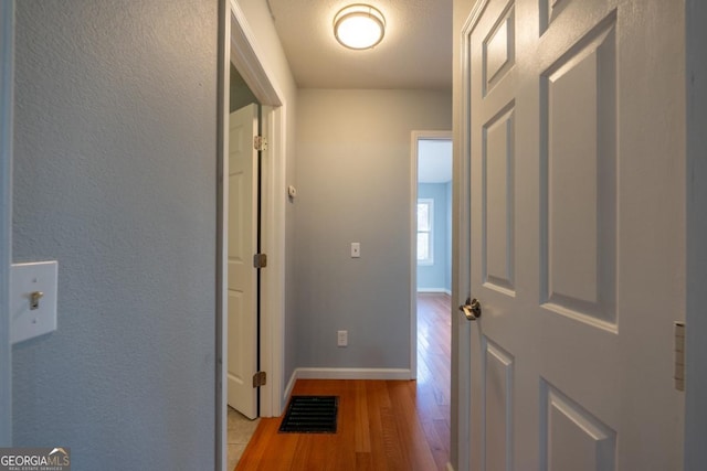 hall with a textured ceiling and light hardwood / wood-style flooring