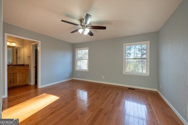 unfurnished bedroom with ceiling fan, wood-type flooring, sink, and ensuite bath