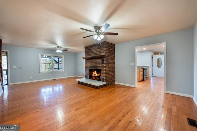 unfurnished living room featuring ceiling fan, a healthy amount of sunlight, light wood-type flooring, and a fireplace