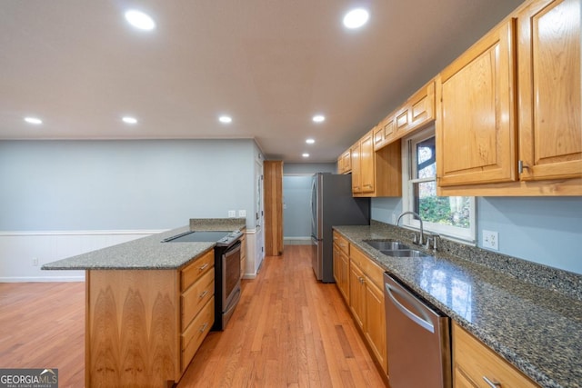 kitchen with appliances with stainless steel finishes, light hardwood / wood-style floors, dark stone countertops, and sink