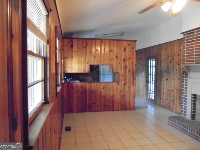 unfurnished living room with lofted ceiling, wooden walls, ceiling fan, light tile patterned floors, and a fireplace