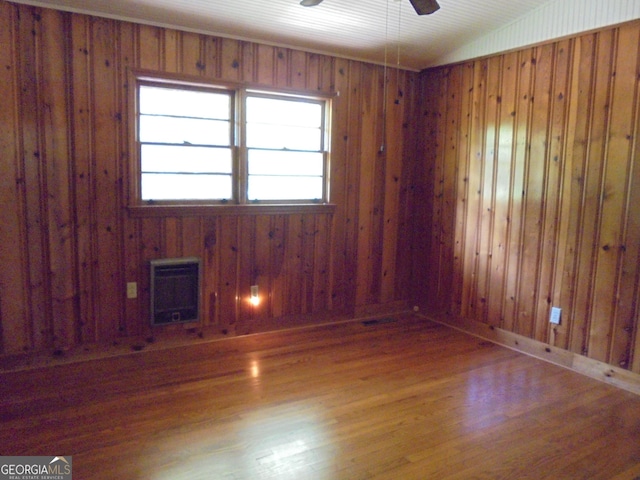 spare room with hardwood / wood-style flooring, heating unit, wooden walls, and vaulted ceiling