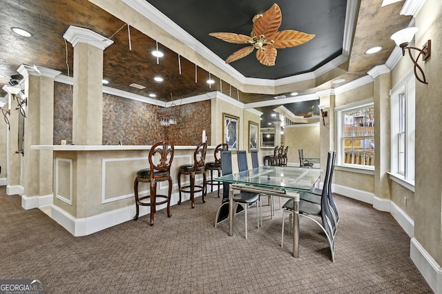 dining room with dark carpet, ornate columns, ornamental molding, a tray ceiling, and ceiling fan