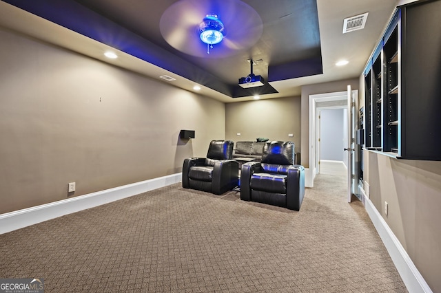 carpeted home theater room featuring ceiling fan and a raised ceiling