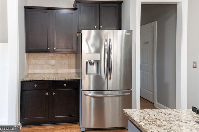 kitchen featuring tasteful backsplash, stainless steel fridge, light stone countertops, and light wood-type flooring