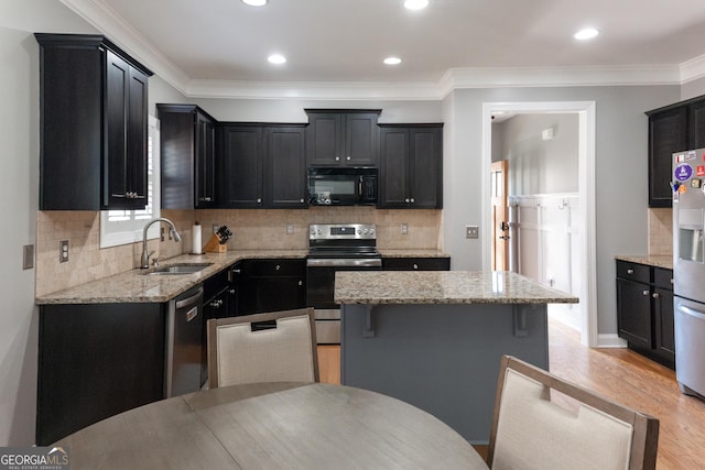 kitchen with light stone countertops, appliances with stainless steel finishes, ornamental molding, sink, and a kitchen island