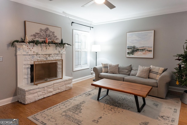 living room with ceiling fan, a stone fireplace, ornamental molding, and light hardwood / wood-style flooring