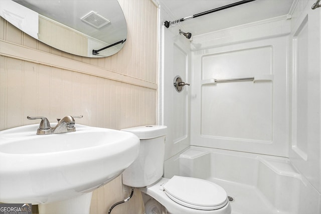 bathroom featuring sink, toilet, a shower, and wooden walls