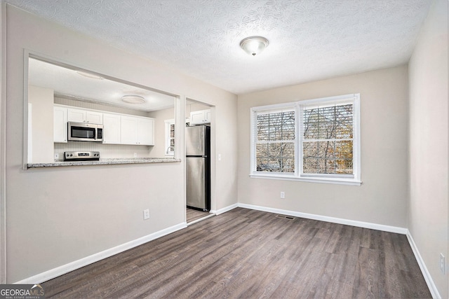 kitchen featuring white cabinetry, dark wood-type flooring, light stone counters, a textured ceiling, and appliances with stainless steel finishes