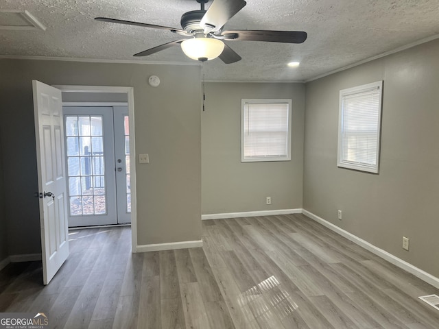 unfurnished room with a textured ceiling, light hardwood / wood-style floors, plenty of natural light, and ornamental molding