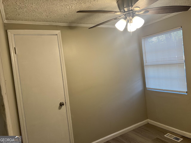 empty room with a textured ceiling, ceiling fan, wood-type flooring, and crown molding