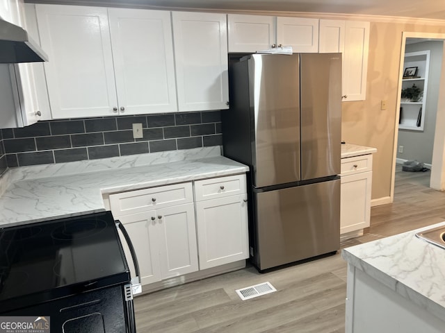 kitchen with stove, light hardwood / wood-style flooring, wall chimney exhaust hood, decorative backsplash, and stainless steel fridge