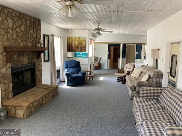 carpeted living room with ceiling fan and a stone fireplace