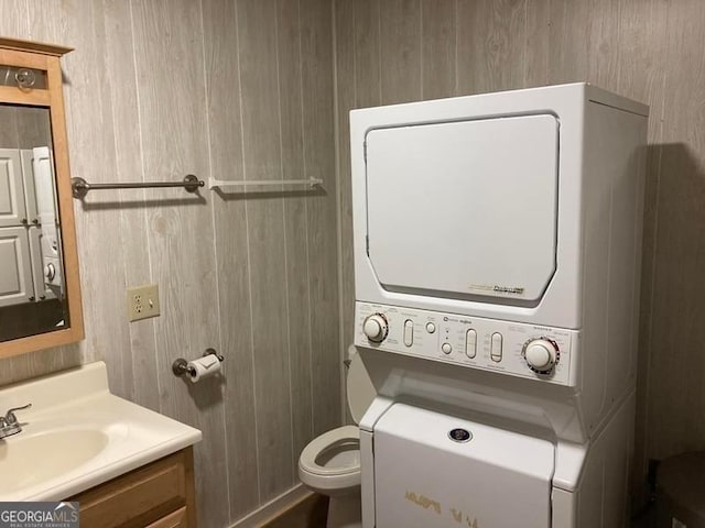 bathroom featuring wooden walls, stacked washer and dryer, vanity, and toilet