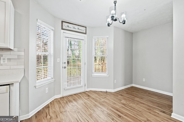 unfurnished dining area featuring a chandelier, a textured ceiling, and light hardwood / wood-style flooring