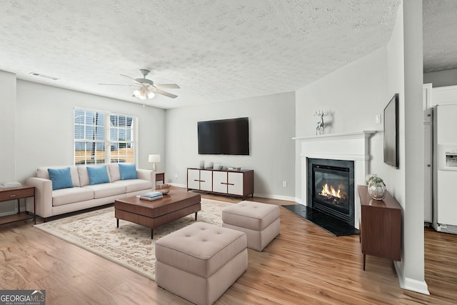 living room featuring ceiling fan, light hardwood / wood-style floors, and a textured ceiling