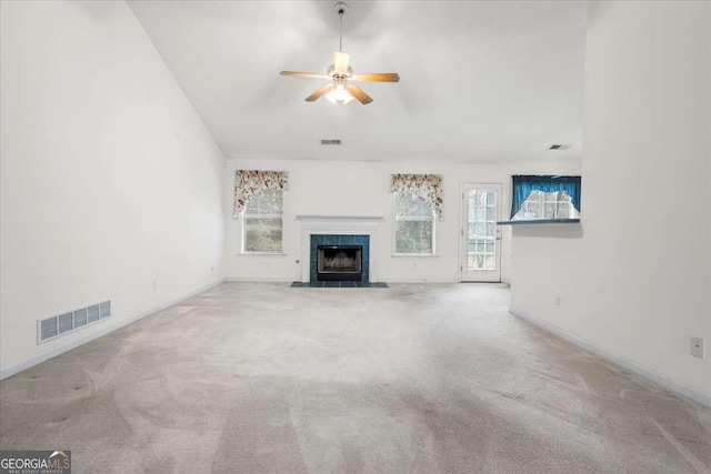 unfurnished living room with ceiling fan, a healthy amount of sunlight, light carpet, and a tile fireplace