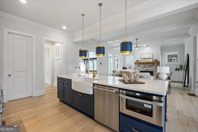 kitchen featuring appliances with stainless steel finishes, ornamental molding, light wood-type flooring, a brick fireplace, and a sink