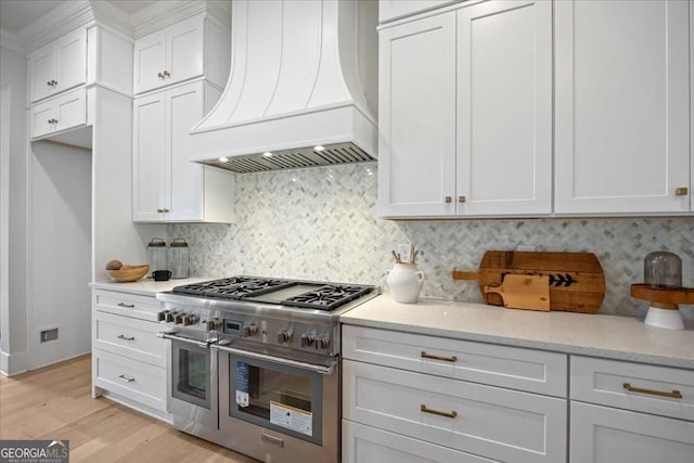 kitchen with range with two ovens, premium range hood, white cabinetry, decorative backsplash, and light wood finished floors