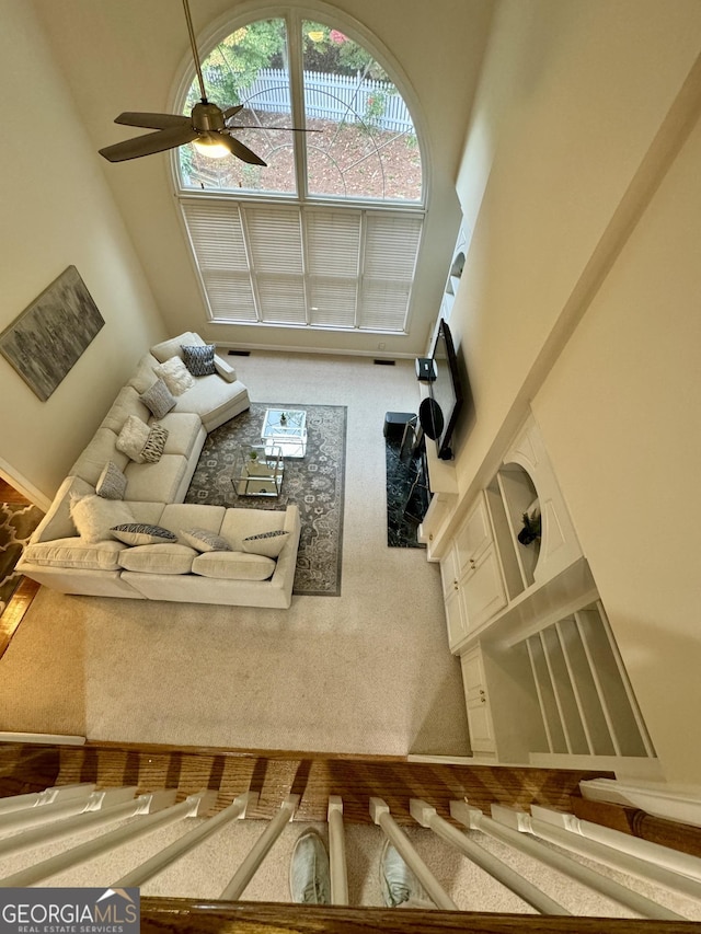 carpeted living room with ceiling fan and a high ceiling