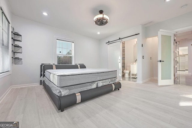 bedroom with connected bathroom, a barn door, and light wood-type flooring