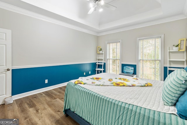 bedroom featuring ornamental molding, a tray ceiling, wood finished floors, baseboards, and ceiling fan