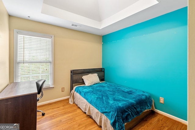 bedroom featuring multiple windows, a tray ceiling, and light hardwood / wood-style flooring