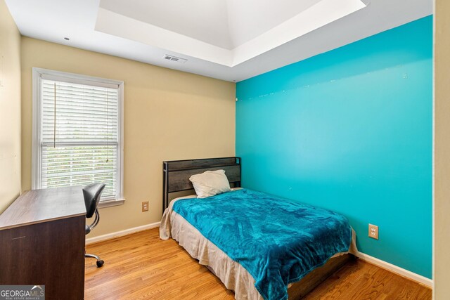 bedroom featuring visible vents, a raised ceiling, baseboards, and wood finished floors