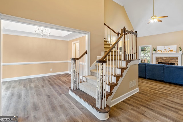 stairs featuring ceiling fan with notable chandelier, ornamental molding, a stone fireplace, and hardwood / wood-style floors