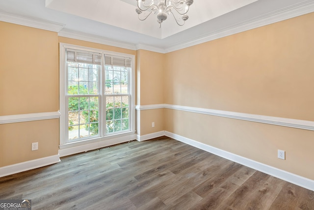 empty room featuring an inviting chandelier, a raised ceiling, and hardwood / wood-style flooring