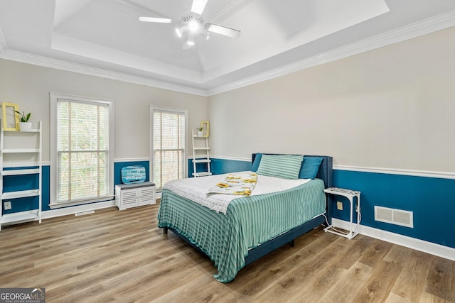 bedroom featuring hardwood / wood-style flooring, ceiling fan, ornamental molding, and a tray ceiling